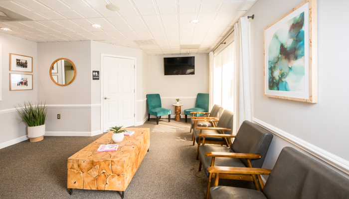 Lincolnton Family Dentistry | Comfortable waiting room with teal chairs, wooden coffee table, and artwork at Lincolnton Family Dentistry