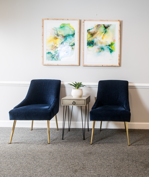Lincolnton Family Dentistry | Two navy blue chairs with gold legs beside a small table and abstract artwork